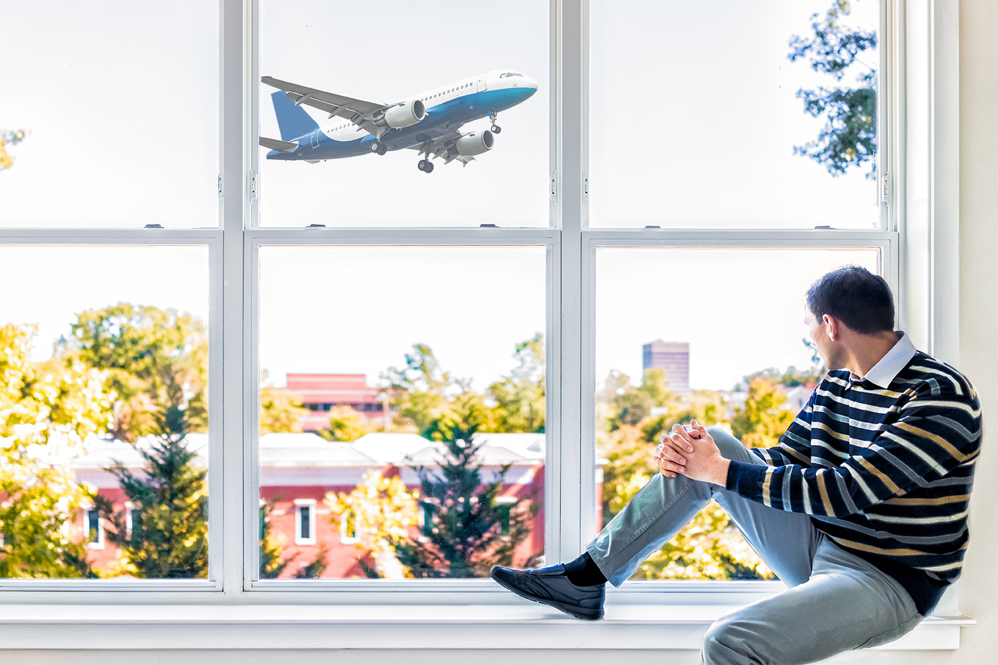 Young man sitting on windowsill by large window overlooking red