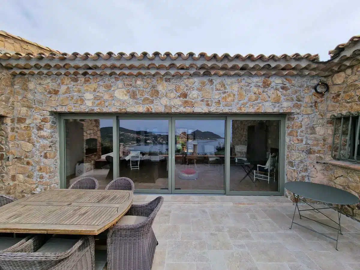 Grande baie coulissante à levage en aluminium Finstral, finition haut de gamme, installée à Agay. Une menuiserie élégante et performante offrant une vue panoramique sur la mer et une parfaite intégration dans une façade en pierre naturelle.